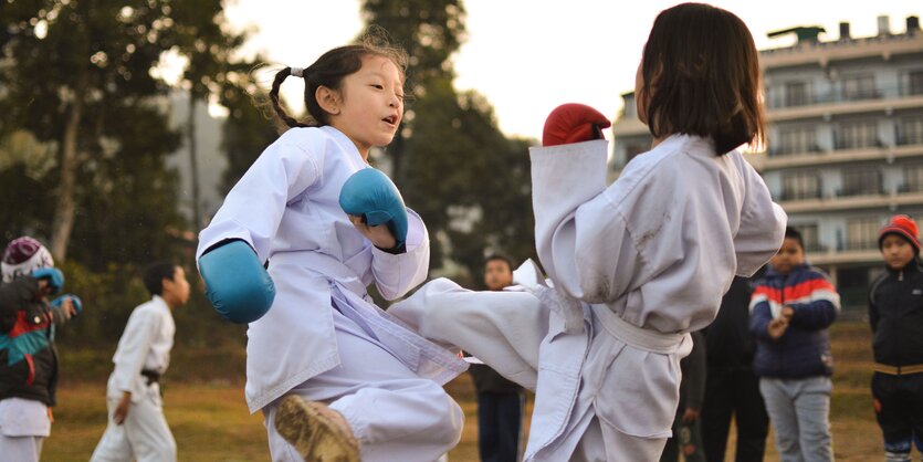 Zwei Mädchen kämpfen Judo mit Boxhandschuhen und weißen Kampfsport-Anzügen gegeneinander