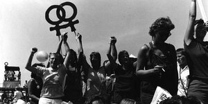 Ein schwarz-weiß Bild zeigt eine Demonstration, Frauen halten ein Plakat mit dem Frauensymbol hoch