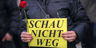 Eine Person hält eine Rose und ein Schild mit der Aufschrift "Schau nicht weg" in der Hand