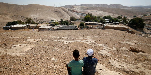 Zwei Jungs sitzen vor einigen Hütten in der Wüste