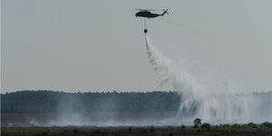 Ein Hubschrauber verteilt Wasser über dem Moor bei Meppen.
