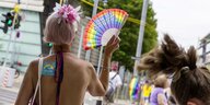 Christopher Street Day in Stuttgart: Ein Mensch von hinten mit einer rosafarbenen Kurzhaarperücke, nacktem Rücken und einem regenbogenfarbenem Fächer