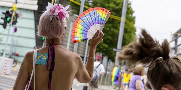 Christopher Street Day in Stuttgart: Ein Mensch von hinten mit einer rosafarbenen Kurzhaarperücke, nacktem Rücken und einem regenbogenfarbenem Fächer Christopher Street Day in Stuttgart: Ein Mensch von hinten mit einer rosafarbenen Kurzhaarperücke, nacktem Rücken und einem regenbogenfarbenem Fächer