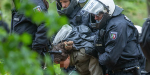 Eine junge Frau wird im Hambacher Forst mit auf dem Rücken verschränkten Armen von mehreren Polizisten abgeführt