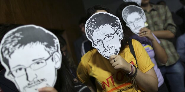 Menschen, die sich aus Pappe ausgeschnittene Masken von Edward Snowden vor Ihr Gesicht halten.