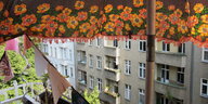 Blick von einem Balkon auf eine Häuserfront, oben begrenzt von einem Sonnenschirm mit Blumenmuster
