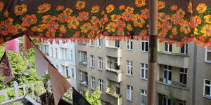 Blick von einem Balkon auf eine Häuserfront, oben begrenzt von einem Sonnenschirm mit Blumenmuster