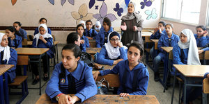 Schulkinder - nur Mädchen - in einem Klassenzimmer, hinten im Raum steht eine ältere Frau und klatscht in die Hände