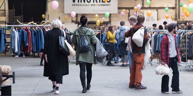 Kleiderständer stehen in einer Halle, Menschen stehen dazwischen.