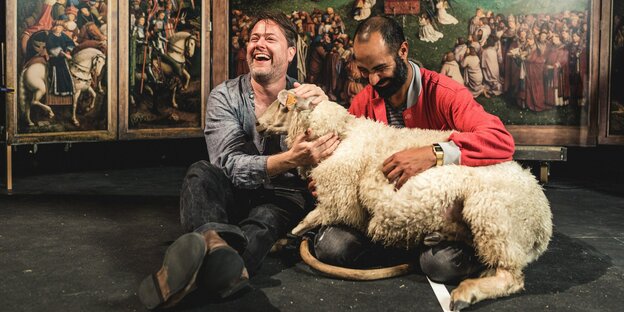 Milo Rau (l.) mit dem Kunst­studenten Bilal Alnouri und einem Schaf vor einer Reproduktion des Genter Altars