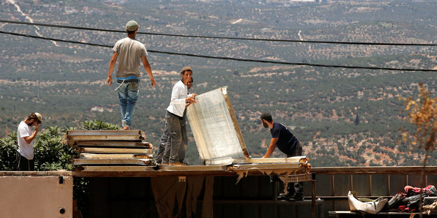 Jüdische Siedler stehen auf einem Dach und reißen das Gebäude ab