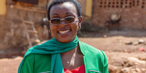 Victoire Ingabire lächelt in die Kamera, sie trägt ein rotes Oberteil und Jacke und Schal in grün