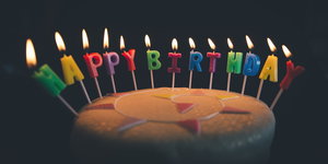 eine Torte, auf der brennende Kerzen den Schriftzug „Happy Birthday“ bilden