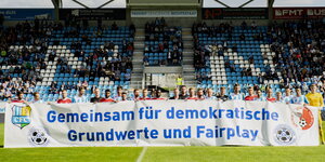 Fußballer stehen auf dem Rasen und halten ein Transparent mit der Aufschrift „Gemeinsam für demokratische Grundwerte und Fairplay“