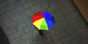 Ein aufgespannter, bunter Regenschirm, von oben betrachtet auf einem nassen Fußbweg.