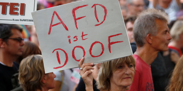 Eine Frau hält ein Schild hoch auf dem steht: AfD ist doof