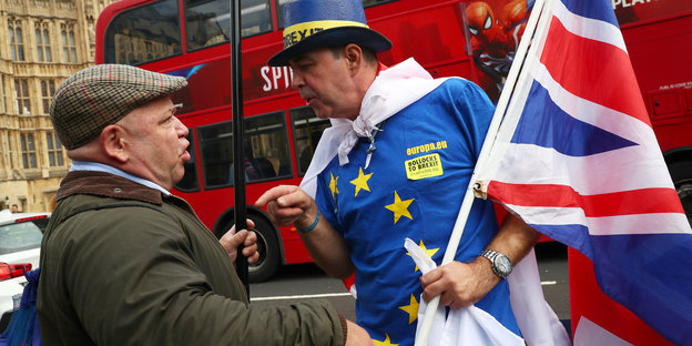 Zwei Männer diskutieren und gestikulieren. Einer von ihnen trägt eine EU- und eine britische Flagge