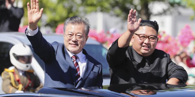 Moon Jae In und Kim Jong Un winken aus einem Auto