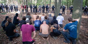 Menschen knien im Wald, davor bilden Polizisten in Uniform eine Kette