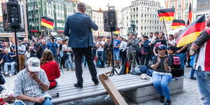 Eine Menschentraube steht mit Deutschlandfahnen vor einem Redner