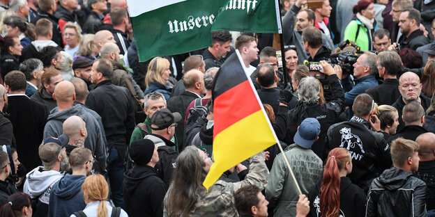 Zahlreiche Menschen drängen sich auf einer Demonstration zusammen, eine Deutschlandflagge wird gezeigt