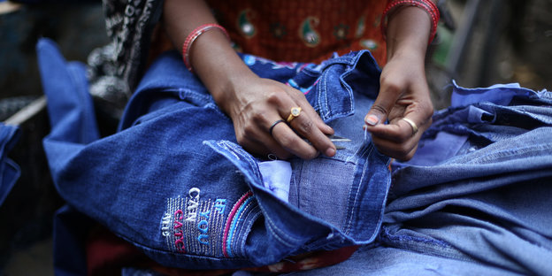 Eine Frau näht Aufnäher auf eine Jeans