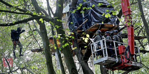 Polizisten nähern sich in einem Hubwagen einem Baumhaus