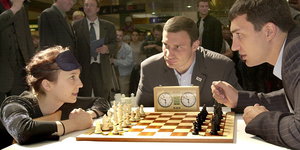 eine Frau und zwei Männer an einem Schachbrett
