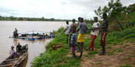 Männer stehen an einem Flussufer und halten einen schwimmenden Fischkäfig an einem Seil fest