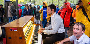 Ein Teilnehmer der Demonstration gegen die Rodung des Hambacher Forsts sitzt im Wald und spielt im Regen Klavier