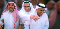 Drei Männer in langen Gewändern stehen nebeneinander und lachen