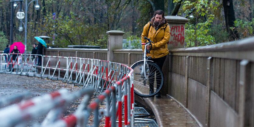 Eine Frau trägt ihr Fahrrad an einer Absperrung entlang