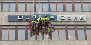 An einem Gebäude mit Schriftzug der Danske Bank seilen sich drei Arbeiter ab
