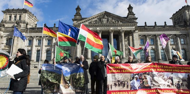 Menschen mit Plakaten und jesidischen Fahnen vor dem Brandenburger Tor
