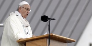 Papst Franziskus in Weiß predigt an einem Stehpult