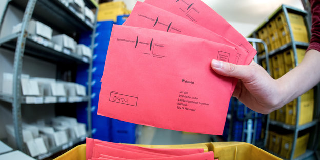 Rote Wahlbriefe in einer gelben Plastikbox.