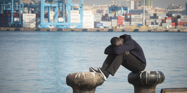 Ein Migrant sitzt am Hafen von Algeciras in Südspanien und hat den Kopf auf die Knie gelegt