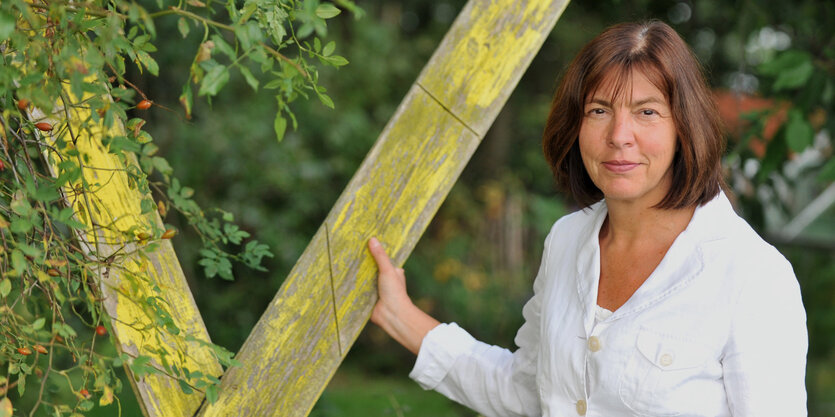 Rebecca Harms steht neben einem gelben Holzkreuz.