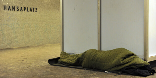 Ein Mensch in Decken schläft in einem U-Bahnhof