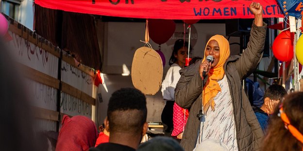 Eine Frau steht auf einem Wagen bei der „We'll Come United“-Demonstration und spricht in ein Mikrofon