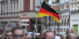 Mehrere Menschen protestieren auf einer Straße, eine Deutschlandflagge wird hochgehalten