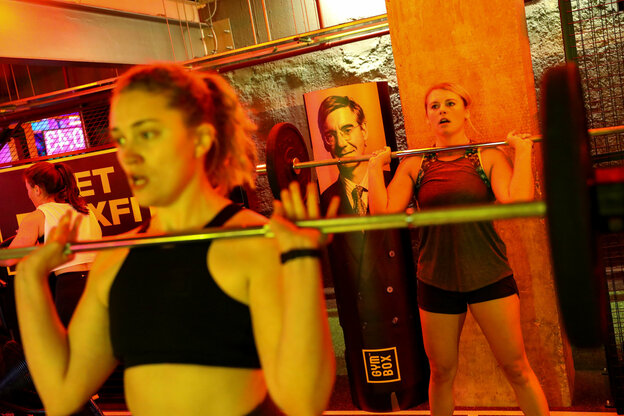 Zwei Frauen stemmen Gewichte im Fitnessstudio, im Hintergrund das Bild vom Politiker Jacob Rees-Mogg