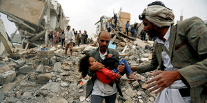 Ein Mann trägt ein Kind aus Trümmern
