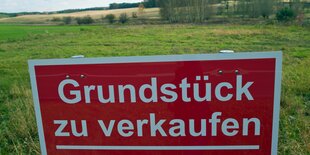 Ein Bauschild auf grüner Wiese mit dem Spruch: Grundstück zu verkaufen