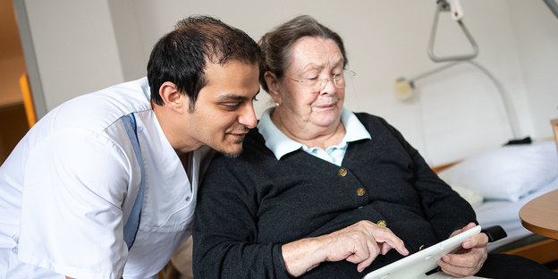 Altenpfleger Amera Kabara schaut in einer Seniorenresidenz mit einer Bewohnerin ein Video an