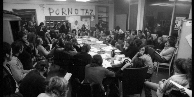 Schwarz-Weiß-Fotos eines voll besetzten Konferenztisches, an eine Wand ist 