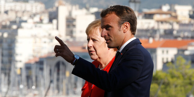 Angela Merkel und Emmanuel Macron stehen nebeneinander und gucken nach links
