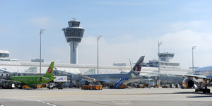 Mehrere Flugzeuge stehen auf dem Flughafen an einem Terminal vor dem Tower in München