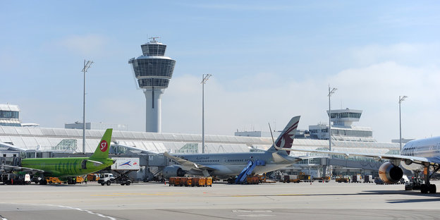 Mehrere Flugzeuge stehen auf dem Flughafen an einem Terminal vor dem Tower in München