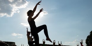 Silhouetten von Menschen, die eine Yoga-Übung im Stehen machen